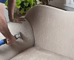 Professional upholstery cleaner deep-cleaning a fabric sofa with a handheld extraction tool and hose in Little Rock, AR.